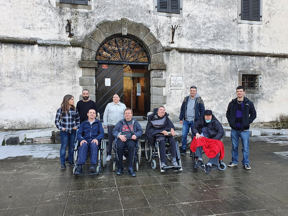 Skupinska slika uporabnikov, spremljevalcev in kustosa pred vhodom v grad. Fotografirano od spredaj.